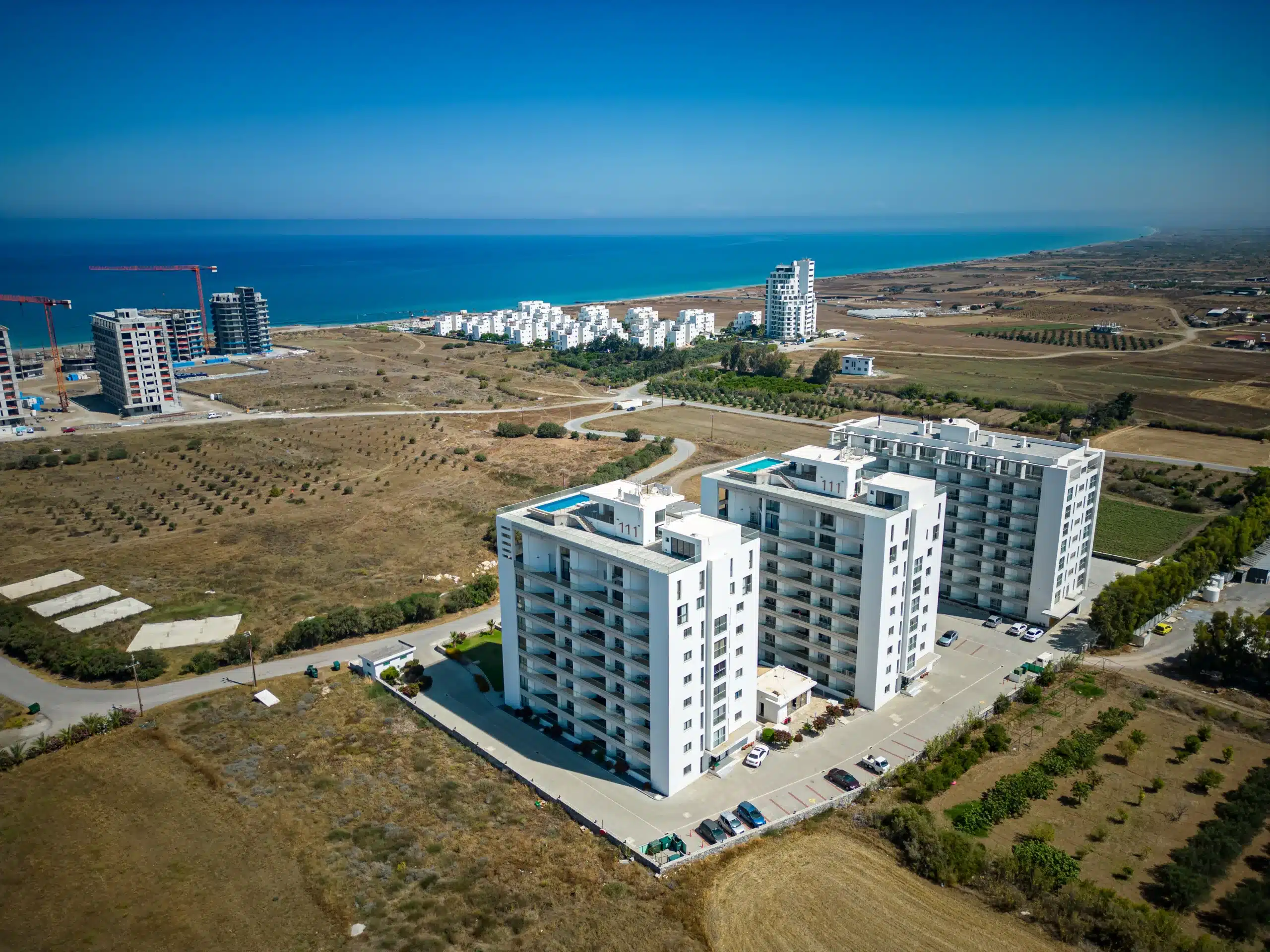 Luftaufnahme einer Neubau-Wohnanlage in Nordzypern mit Dachpools, im Hintergrund der Strand und das Meer